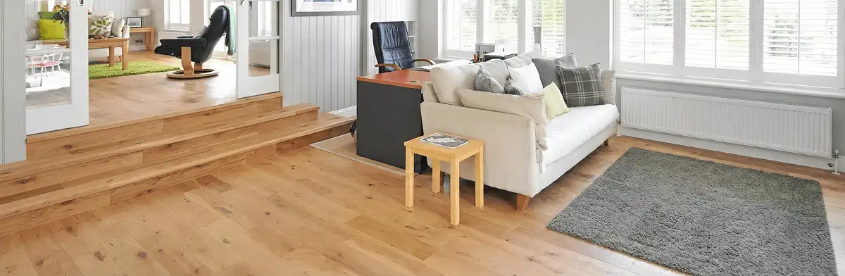 A modern living room with professionally installed laminate flooring, a beige sofa, a small side table, a gray rug, and large windows with white shutters in Nashville, TN